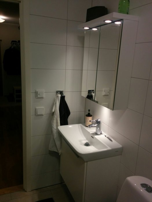 Ett badrum med en tvättställ och spegelskåp med tre spotlights ovanpå.