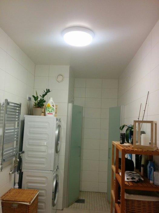 Ett upplyst badrum med takarmatur, tvättmaskin, torktumlare och badrumsmöbler.