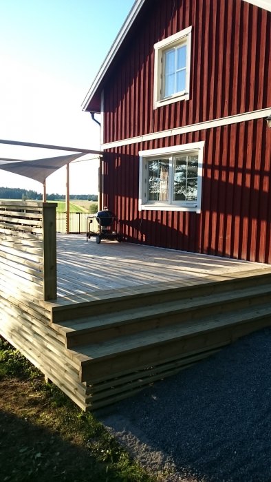 Nybyggd träaltan vid rödfärgat hus med vita fönster och en grill på altanen.