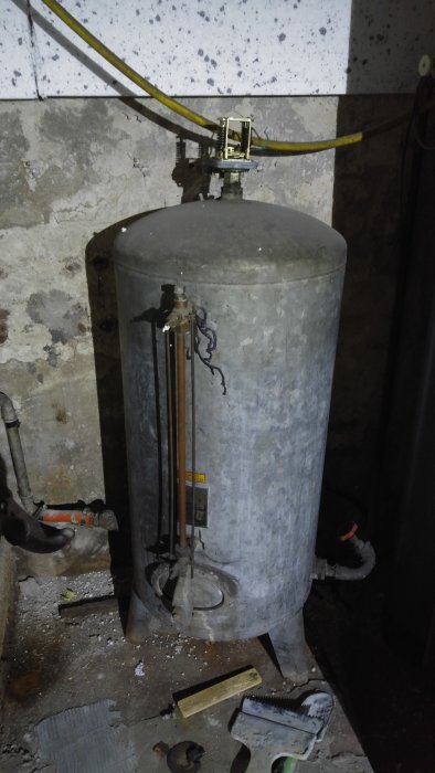 En 130-literstank i ett källarrum, med röranslutningar och mätare, möjlig hydropress eller hydrofor.