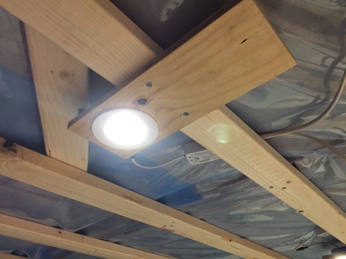 Installation av takspotlight i träbjälklag med isolering och plastfolie, inkluderat kablar och drivdon.