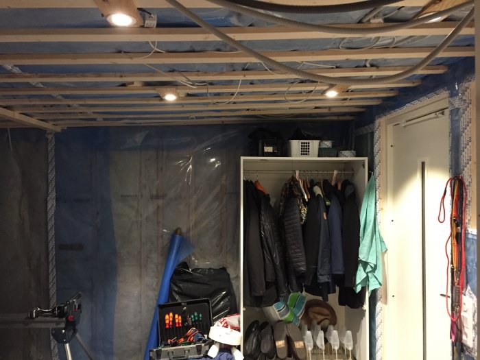 Renoverad hall med isolering, pågående installation av LED-spottar i taket, med verktyg och garderob synligt.