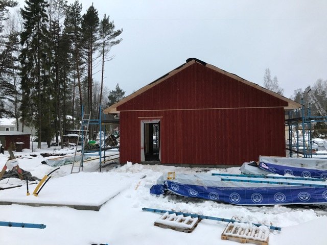 Nytt tak monterat på rödmålat hus, byggmaterial och snö runtomkring.