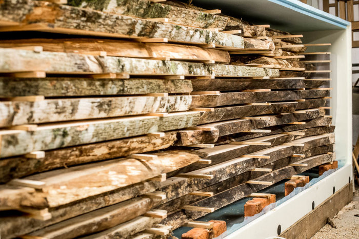 Stacked rough-cut lumber in a kiln ready for drying, showcasing various wood species and natural patterns.