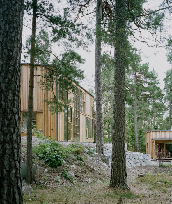 Nybyggd huvudbyggnad och attefallshus i trä, omgiven av tallar och bergig terräng.