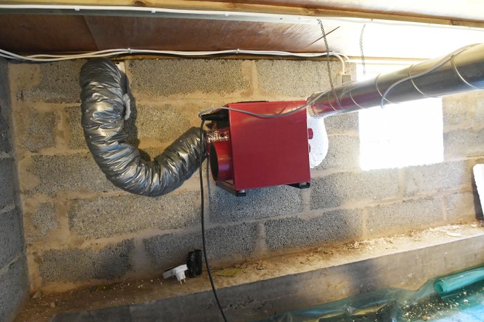 Installation av flexibel ventilationsslang kopplad till röd ventilationsenhet i ett utrymme med gråa blockväggar.