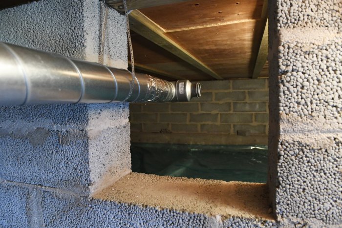 Metallventilationsrör som passerar genom en vägg med isolering och in i en träklädd utrymme.