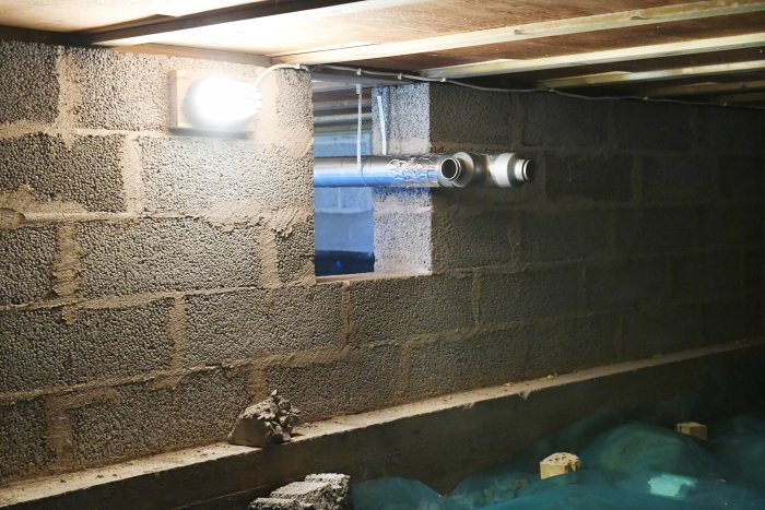 Ventilationsrör och elledningar i en källare med oputsade betongblocksväggar.