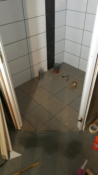 Delvis lagd klinker i ett badrumsprojekt som visar olika nyanser på varje rad, verktyg och tiling tillbehör på golvet.