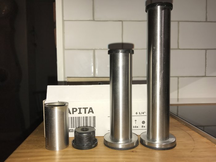 Metallrör i olika längder med en plastplugg upptill, placerade på en träyta framför en kakelvägg.