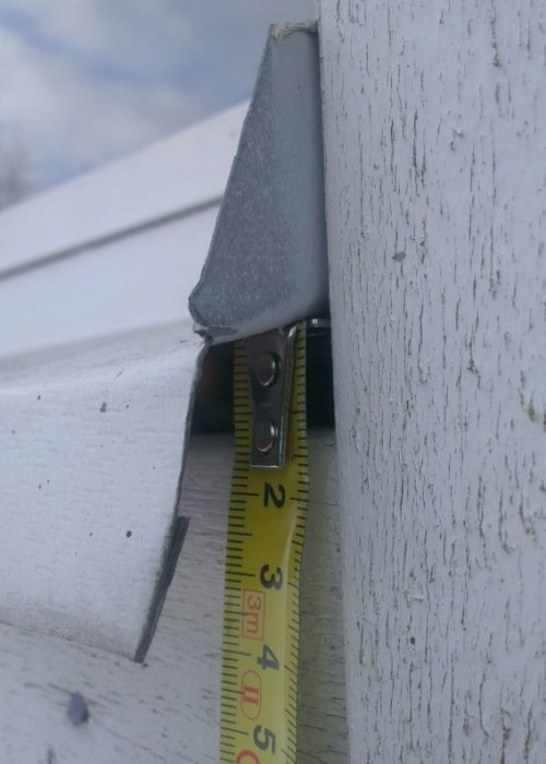 Mätning av glapp mellan fönsterbleck och vertikalt foder på ett hus, med ett måttband som visar över 10 mm utrymme.