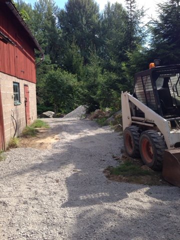 Nygrusad uppfart med bobcat vid nymålat rött hus omgivet av träd.