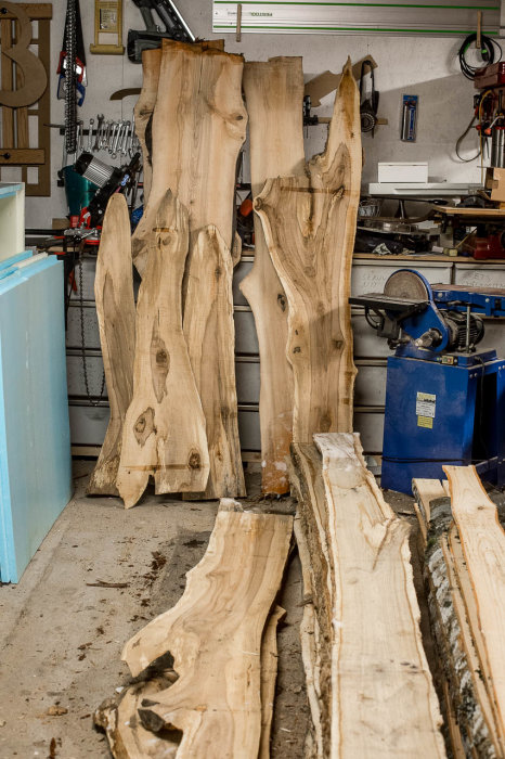 Utsågade träplankor av olika former torkar i en verkstad, potentiellt för ett matbord.