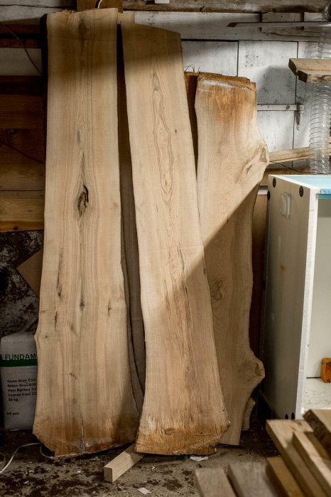 Träplankor i torkprocess i ett verkstadsutrymme, förberedda för att bygga ett matbord.