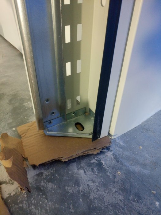 Detaljbild av en garageportskena som inte når ner till golvet, skenans fäste syns nära betonggolv.