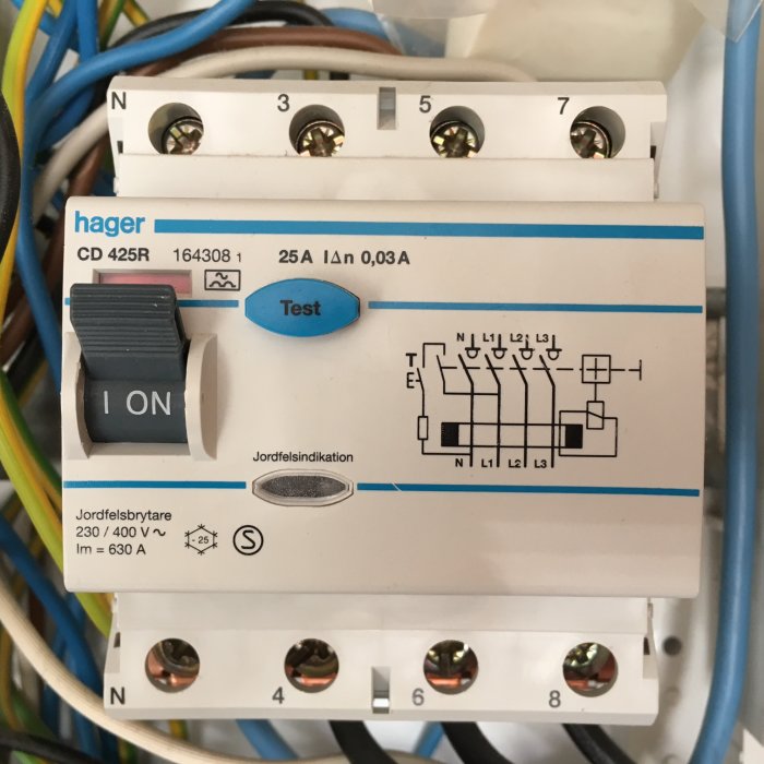 Närbild på en jordfelsbrytare med testknapp och schema, omringad av elektriska kablar.