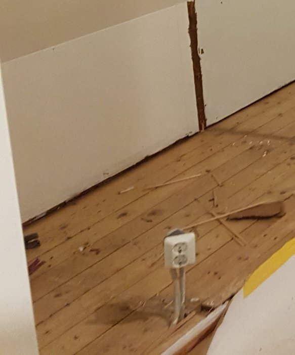 Fritt hängande eluttag mitt på ett trägolv där en vägg tidigare tagits bort, med synliga kablar och väggrester.