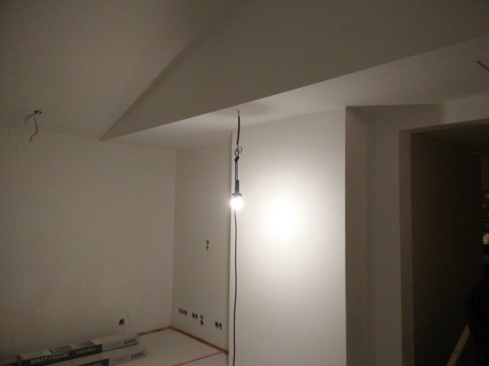 Nyputsad vit murstock i ett rum under renovering, med släta ytor och en hängande lampa.