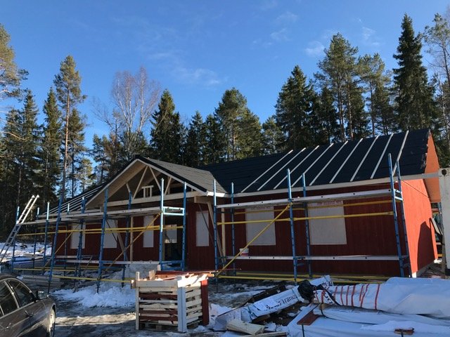 Nytt tak ovanför veranda under konstruktion vid röd husfasad, med ställningar och snö på marken.