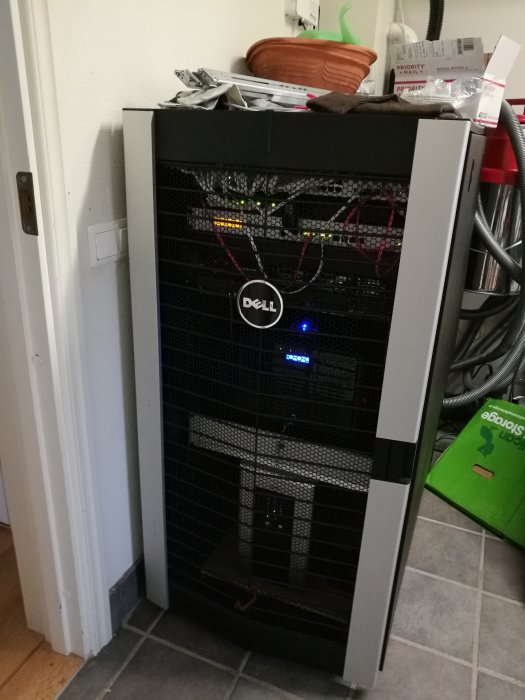 Dell-serverrack i en tvättstuga med synliga kablar och nätverksutrustning, ovanpå diverse föremål.