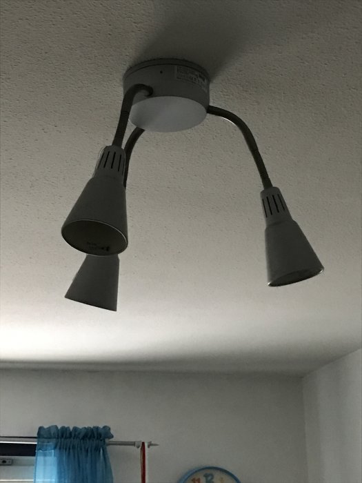 Takkrona med två grå lampskärmar, utan synliga skruvar, fastsatt i taket med tre små hål synliga.