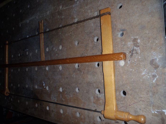 Traditional hand saw with a wooden handle and a blade, leaning against a pegboard wall.