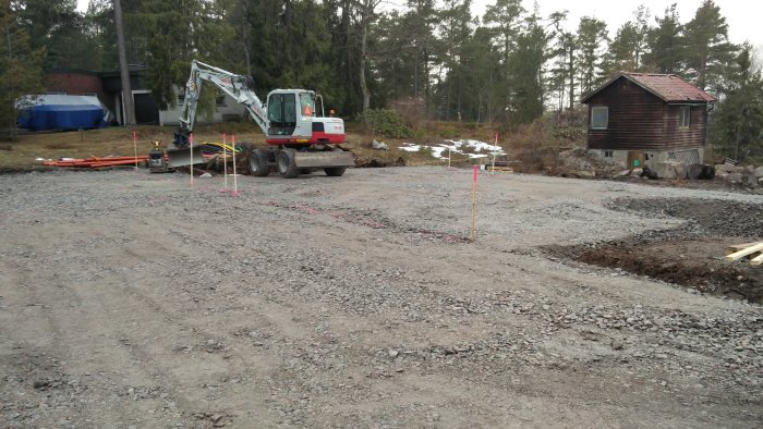 Grusfylld byggplats med komprimerad mark och grävmaskin, förberedd för dränering och infrastruktur.