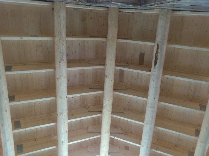 Innertak av trä med synliga takstolar och läkt i ett oisolerat timmerhus.