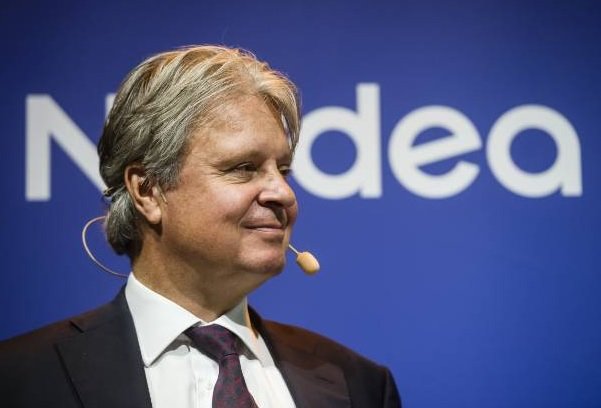 Leende man i kostym framför Nordea-logotypen med mikrofonheadset.