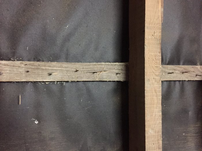 Vindpapp och spikreglar på en vägg med träpanel som saknas, visar konstruktionen.