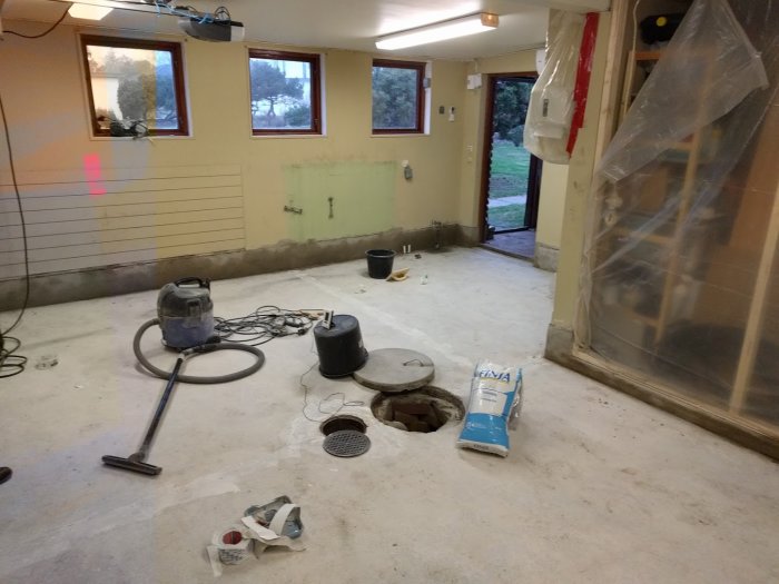 Ett garage under renovering med verktyg, spackel och en dammsugare på det nakna betonggolvet.