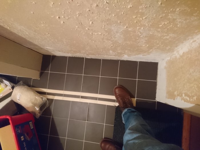 Ej färdigställd hall med oslipade väggar och grå klinkergolv, person i bild.