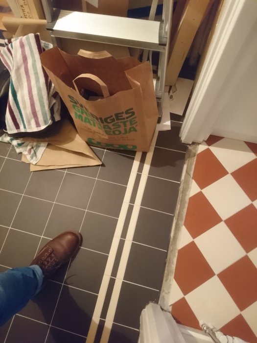 Oavslutad hallrenovering med golvkakel och en papperskasse bland byggmaterial.