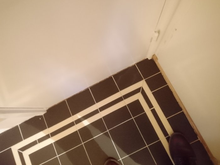 Icke färdigställd hall med svartvitt kakelgolv och vit vägg, överväger kakel i nischen.