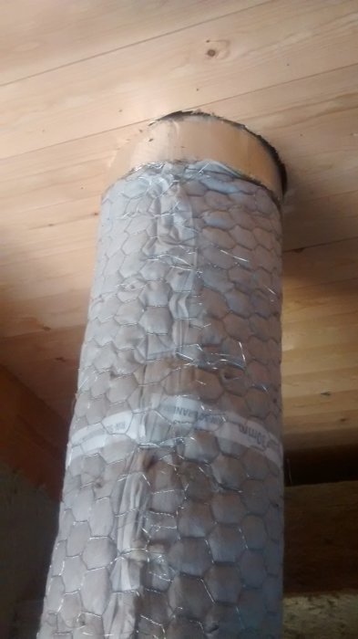 Ventilationsrör omgivet av isoleringsmaterial mot en trävägg.