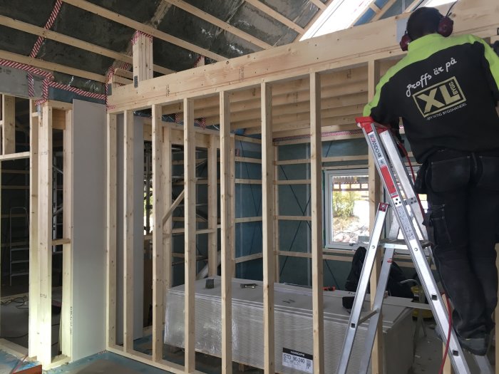 Arbetare reglar upp en innervägg i ett hus med isolering synlig i väggarna.