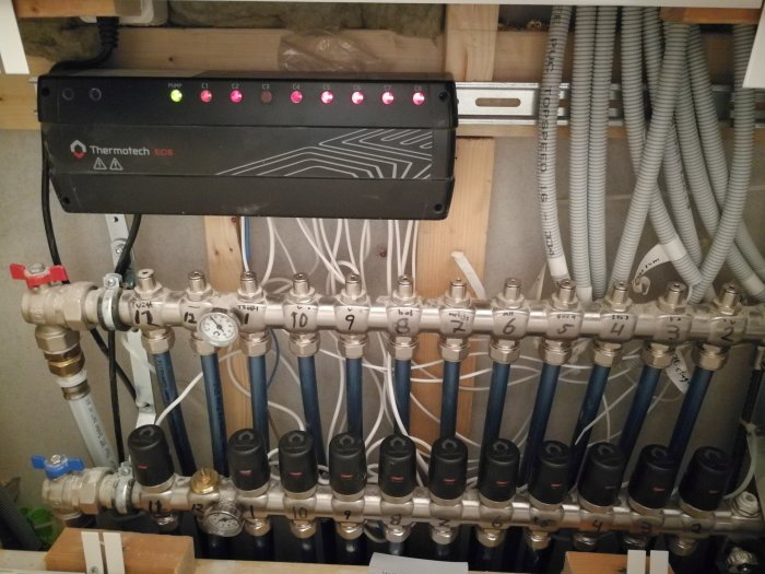 Golvvärmefördelare med termostater och en Thermotech ECB styrenhet, indikerar potentiellt problem med systemet.
