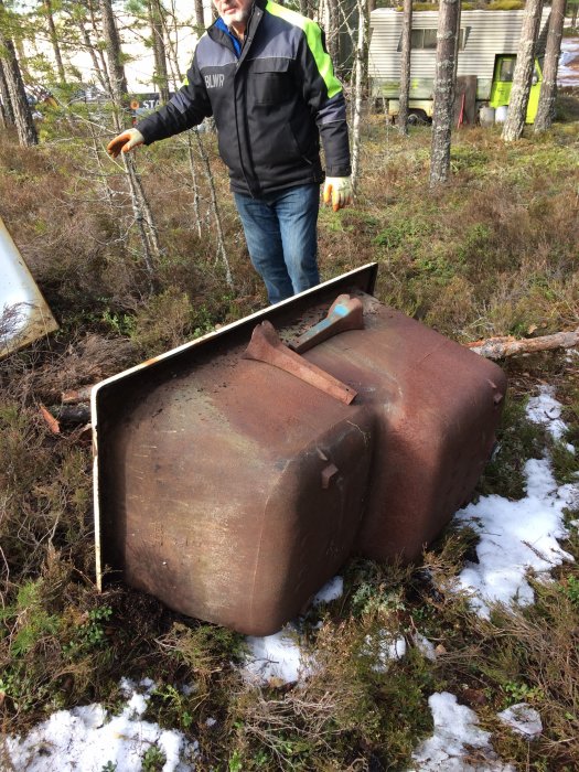 Person vid ett gammalt, rostigt badkar och toalettstol utomhus med snö och vegetation i bakgrunden.