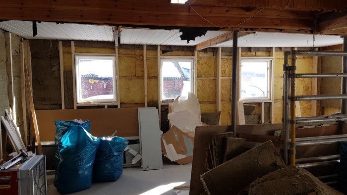 Renoveringsarbete inuti ett hus med exponerad isolering och ojämna fönster.