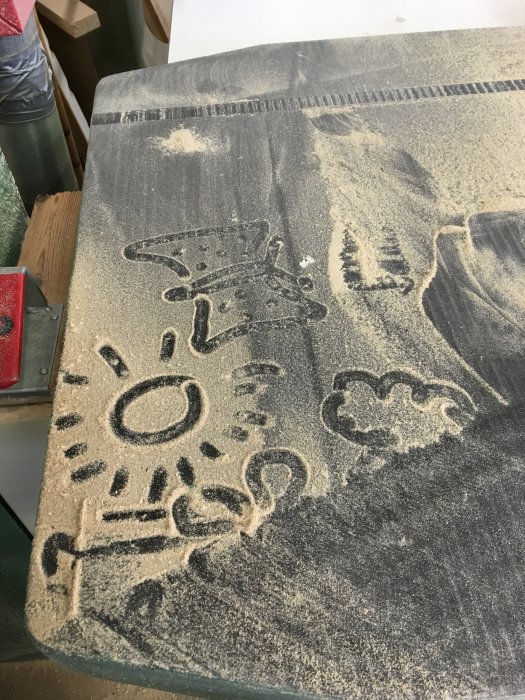 Grafitti av sågspån på en bandsåg visande figurer och mönster, indikerar behov av dammhantering.
