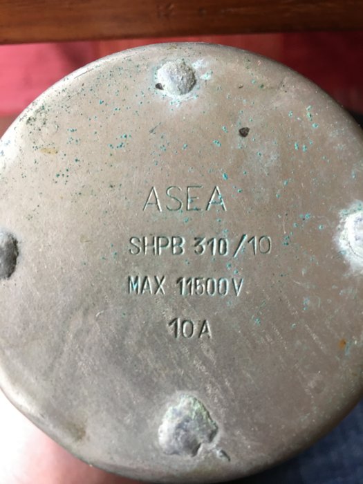 Närbild på en metallända av en objekt med texten "ASEA SHPB 310/10 MAX 11500V 10A", eventuell gammal rörsäkring.