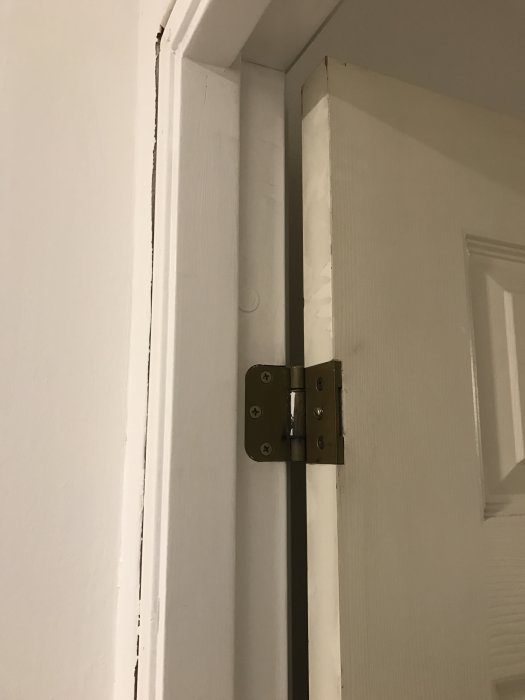 Gångjärn och karmdetalj av en vit innerdörr som är en del av en fråga om byte till nya dörrar.