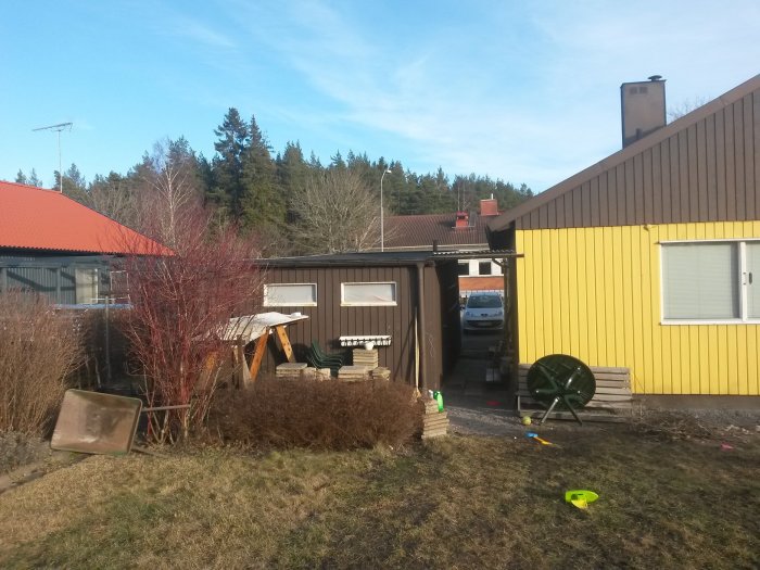 Gult hus med brunt garage och carport, leksaker på gården, tänkt tillbyggnadsområde markeras av gängstig.
