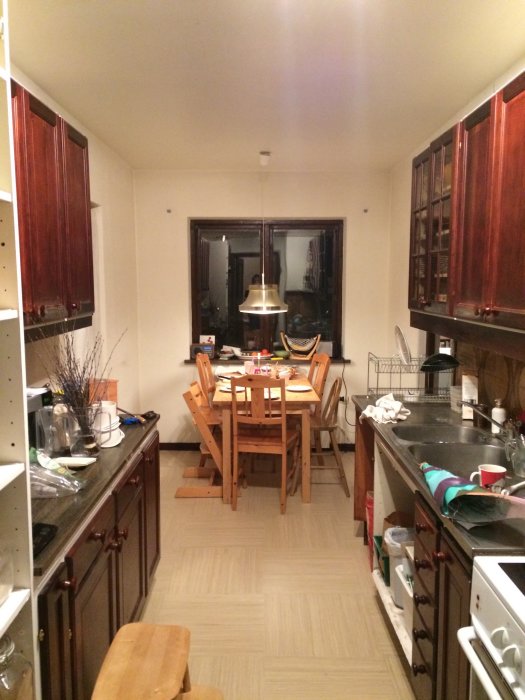 Köksinteriör i 70-talsstil med mörka trädörrar, vit diskbänk och matbord med stolar, redo för renovering.
