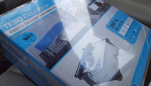 En ny TEBO Ceramica elektrisk kakelskärare i förpackning, 550 W, köpt från Beijer, ligger på ett bilsäte.