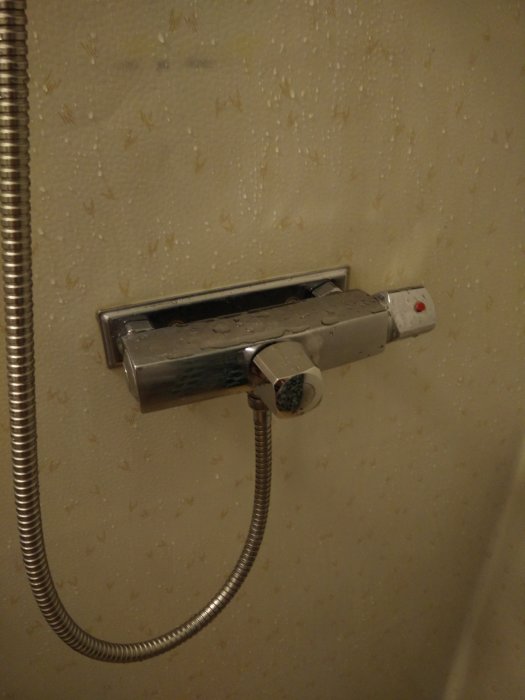 Väggmonterad duschblandare med slitage och ansluten duschslang, behöver identifiering och underhåll.