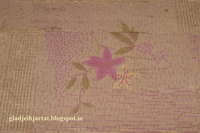 Mönstrad tapet med blommor i rosa och lila nyanser framför strukturer med flera lager gamla tapeter.