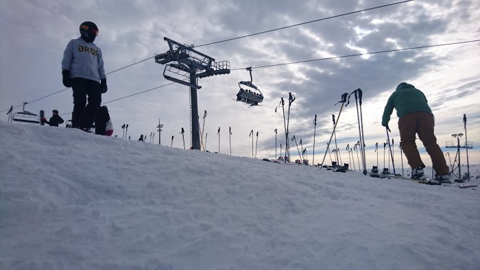 Skidbacke i Sälen med skidåkare, skidlift och nedslagna skidstavar i förgrunden.