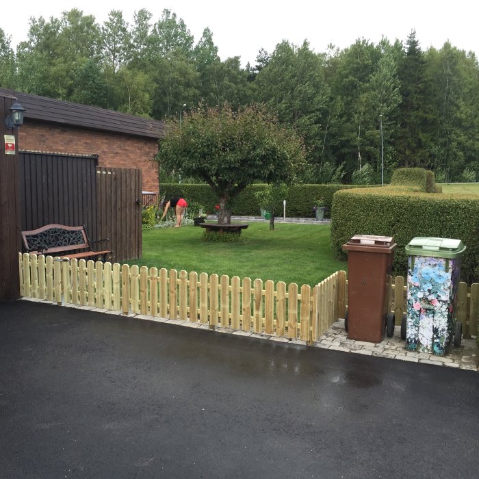 Trädgård med nybyggt staket till vänster och person som arbetar i bakgrunden.