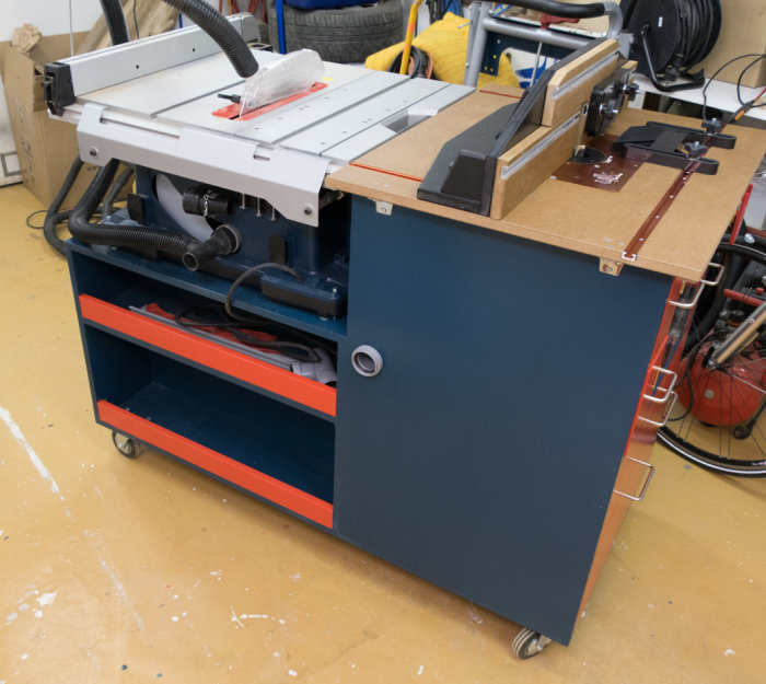 Blå och röd verktygsvagn med inbyggda såg- och fräsbord av märket Bosch i ett garage.
